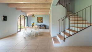 A spacious living area with a dining table and chairs, a staircase with a metal railing, and a large window providing natural light. - Apartment Azzurro- Cignella Resort Tuscany (Trequanda)