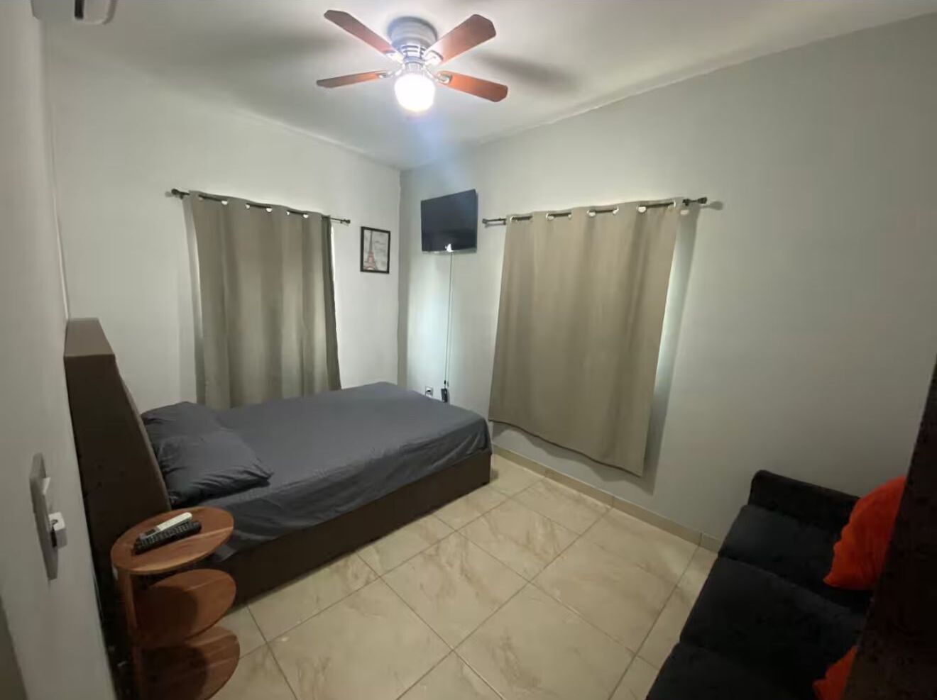 A bedroom with a bed, a ceiling fan, curtains, a TV, and a small table.
