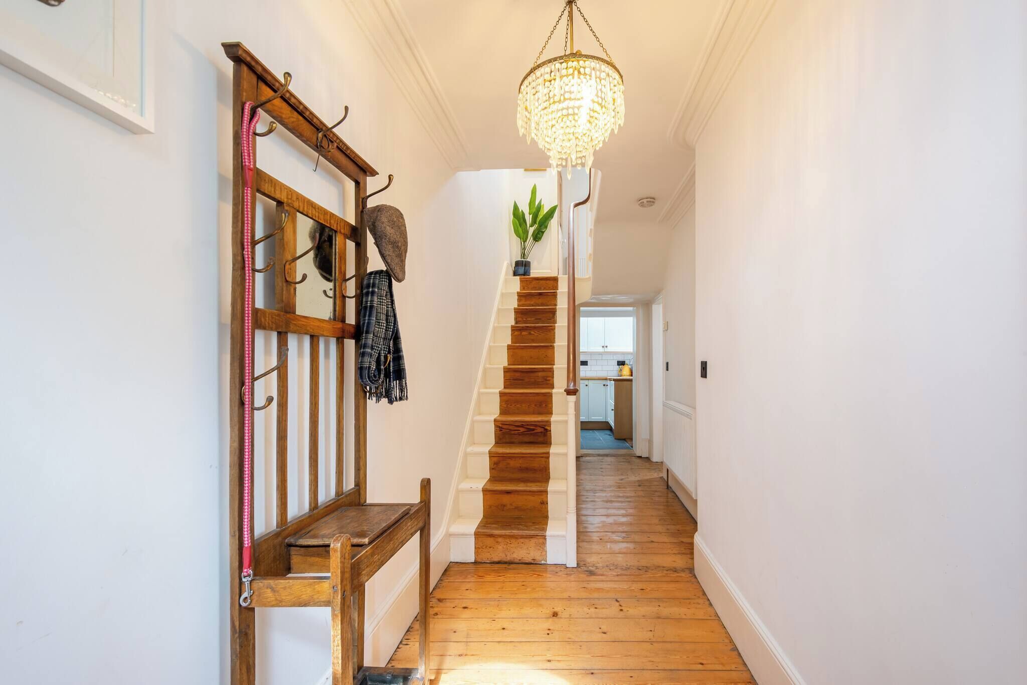 A wooden staircase with a chandelier, a bench, and a plant on the landing.