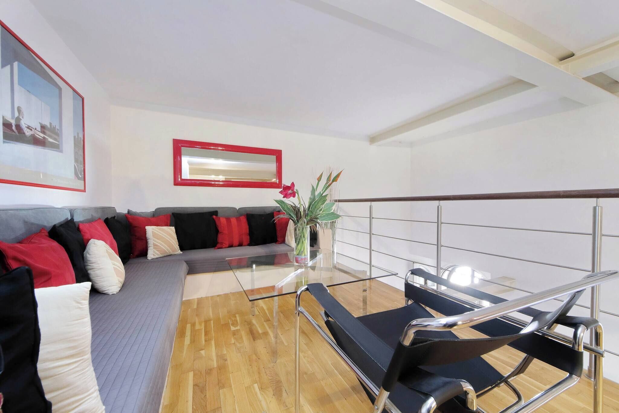 Een moderne woonkamer met een glazen salontafel, een bank met rode en zwarte kussens, een zwarte fauteuil en een potplant.