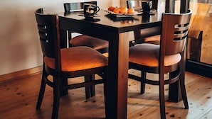 Un coin repas avec une table en bois et quatre chaises, une assiette de fruits et une tasse de café.