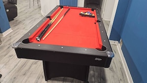 A pool table with a red felt surface, pool cues, and balls. - A very peaceful home (Oshawa)