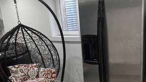 A modern kitchen with a stainless steel refrigerator, a hanging chair with floral cushions, and a window with blinds. - A very peaceful home (Oshawa)