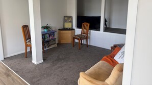 Un salon avec un canapé, deux fauteuils, une bibliothèque, un téléviseur et une fenêtre.
