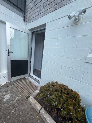A white brick exterior with a sliding glass door, a small window, and a security camera. - Cozy 2-Bedroom House Rental in Whangārei, New Zealand (Whangārei)