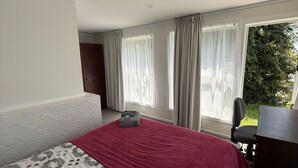 Une chambre d’hôtel avec un grand lit, un bureau et une vue sur la verdure environnante.