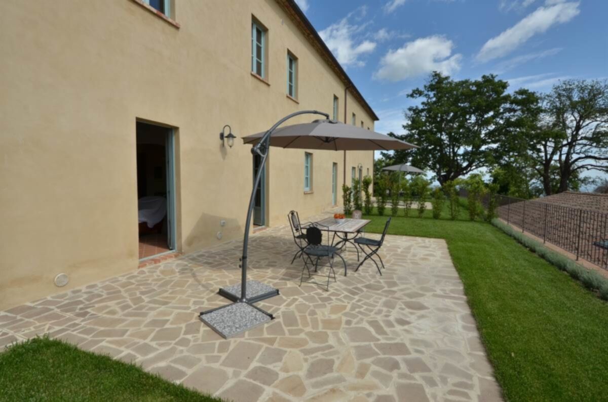 Eine Terrasse mit Tisch und Stühlen, einem schattenspendenden Sonnenschirm und einem Steinboden.