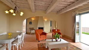 Un vaste espace de vie comprenant une table à manger, deux fauteuils orange, une table basse blanche et une cheminée.
