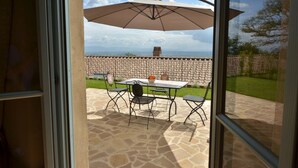 Une terrasse extérieure avec une table et des chaises, un grand parasol et un mur de pierre en arrière-plan.