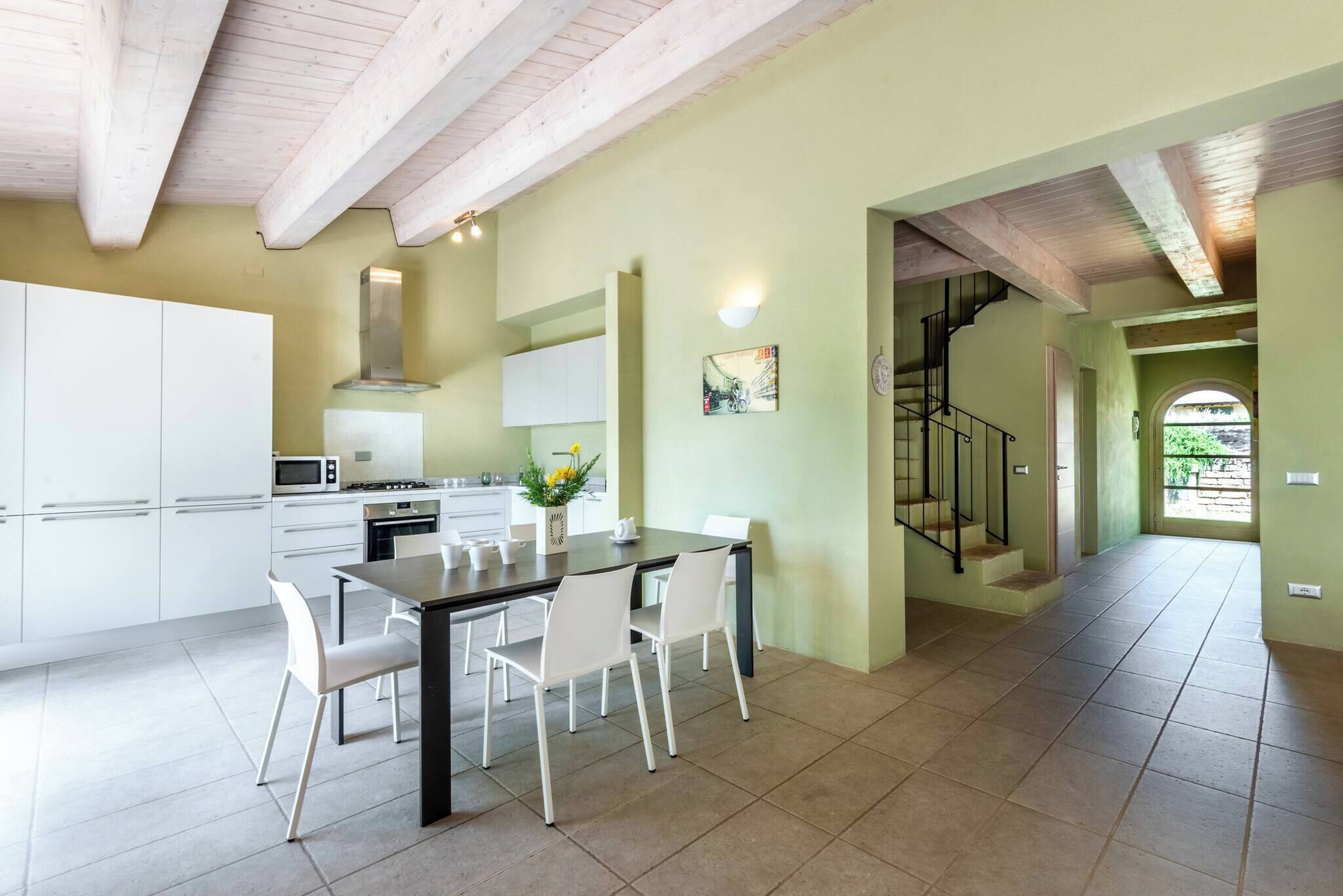 Une cuisine moderne avec des meubles blancs, une table à manger avec des chaises et un escalier menant à l’étage supérieur.