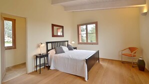 Quarto com cama, mesas de cabeceira, uma cadeira e uma janela.