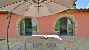 Um pátio com uma mesa, cadeiras, um guarda-sol e um muro de tijolos com portas em arco.