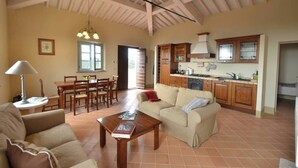 A spacious living area with a dining table and chairs, a sofa, and a kitchen with wooden cabinets and a tiled floor. - Quercia Apartment - Cignella Resort Tuscany (Trequanda)