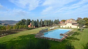 A swimming pool surrounded by a well-maintained lawn, with a view of distant hills and trees. - Quercia Apartment - Cignella Resort Tuscany (Trequanda)