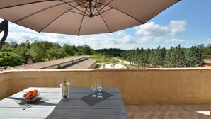 A balcony with a table, an umbrella, and a view of a vineyard. - Quercia Apartment - Cignella Resort Tuscany (Trequanda)