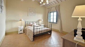 A bedroom with a bed, bedside tables, a chandelier, a window with curtains, and a wall decoration. - Quercia Apartment - Cignella Resort Tuscany (Trequanda)
