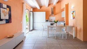 A modern kitchen with white cabinets, a dining area with white chairs, and a large window. - Villa Pesca amazing House in the heart of Tuscany (Tuscany City)