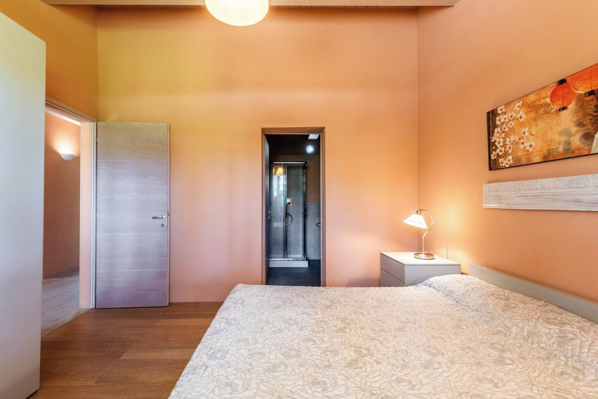 Une chambre à coucher comprenant un lit, une table de chevet, une porte et un couloir menant à une salle de bain.