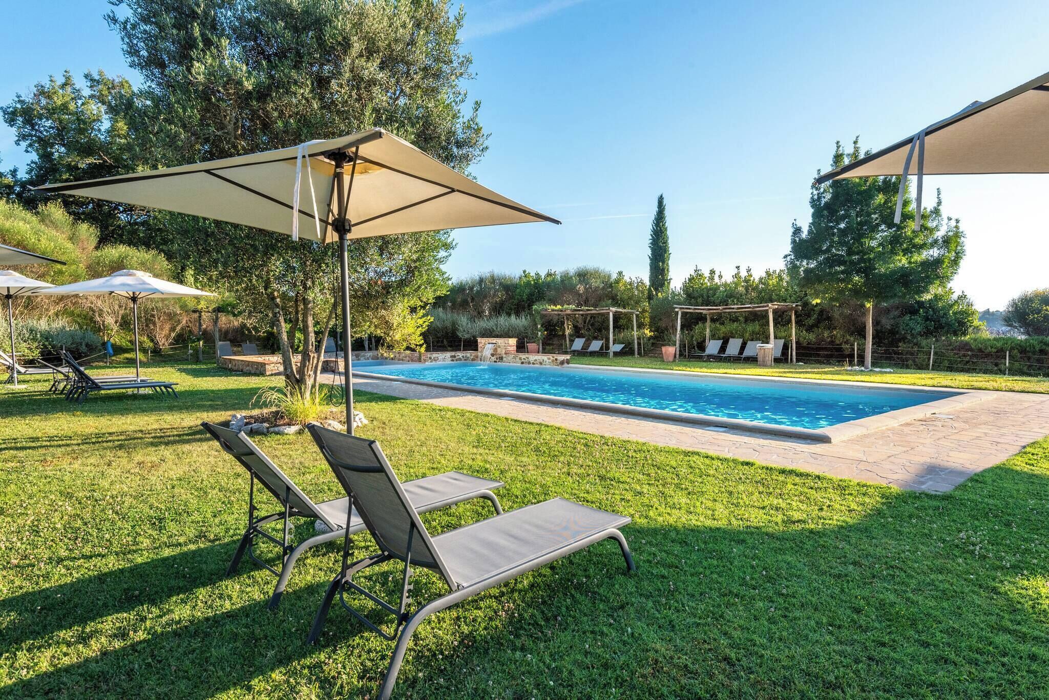 Ein Swimmingpool mit Liegestühlen und Sonnenschirmen, umgeben von einem gepflegten Rasen und Bäumen.