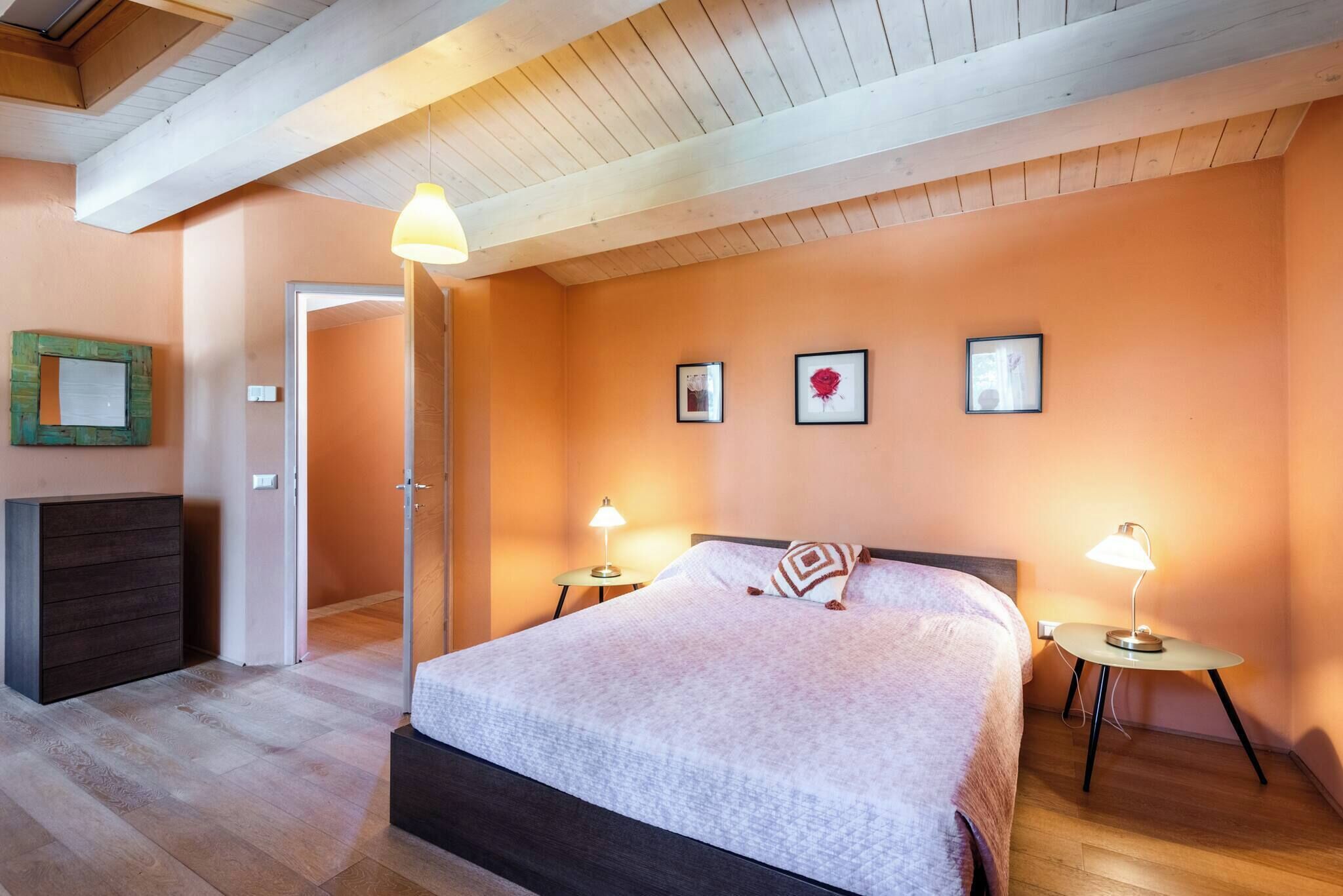 Ein Schlafzimmer mit einem Bett, zwei Nachttischen mit Lampen, einer Kommode und einer Tür zu einem anderen Raum.
