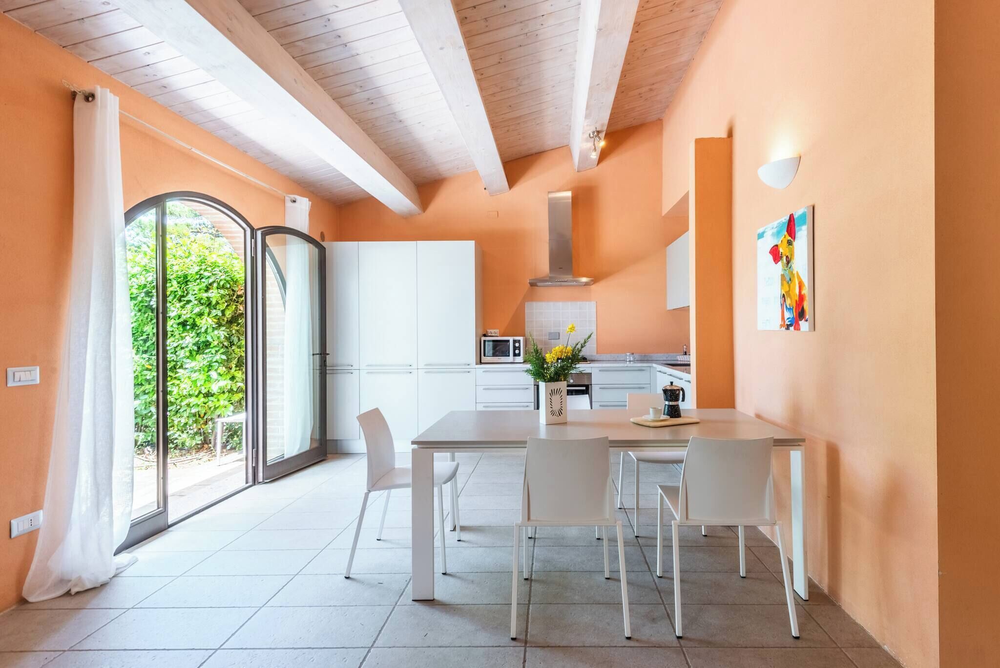 A modern kitchen with white cabinets, a dining table with chairs, and a large window with curtains.