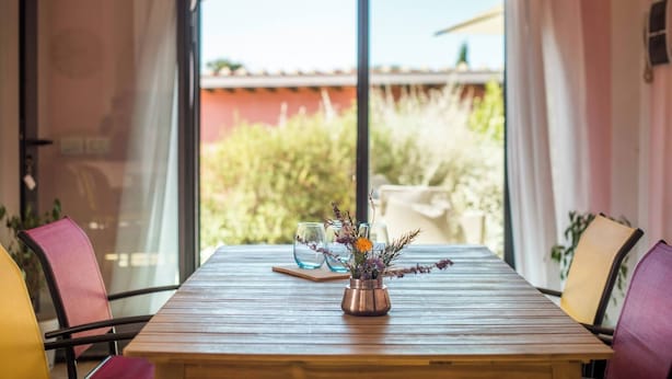 A wooden table with a copper vase of flowers, two glasses, and a wooden board.