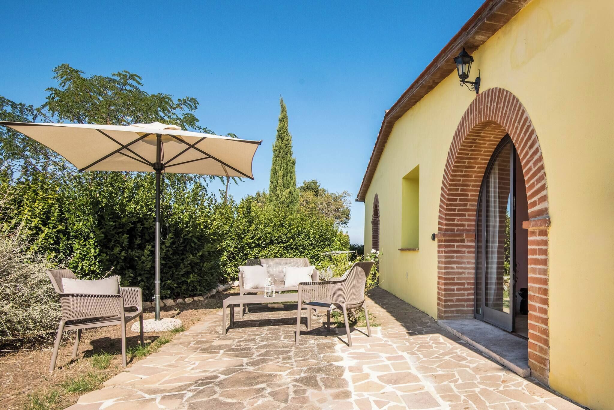 Une terrasse extérieure avec un sol en pierre, une table, des chaises et un grand parasol.