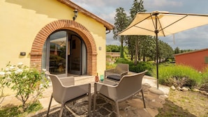 An outdoor patio with wicker furniture, a large umbrella, and a brick archway leading to a glass door.