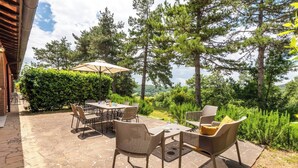 Eine Terrasse im Freien mit Steinboden, Korbmöbeln und einem Tisch mit Stühlen.