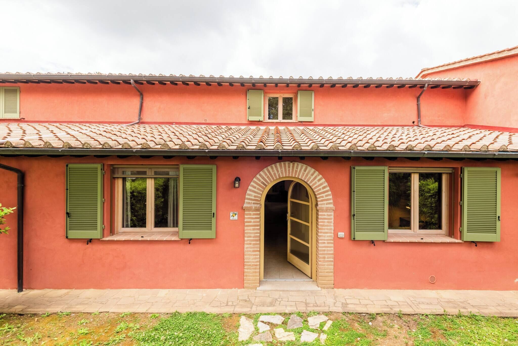 Un bâtiment à la façade rouge, aux volets verts et au toit recouvert de tuiles.