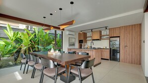A modern kitchen with wooden cabinets, a central island, and a dining area with a large table and chairs. - Villa Pasisi 11 - Canggu (Canggu)