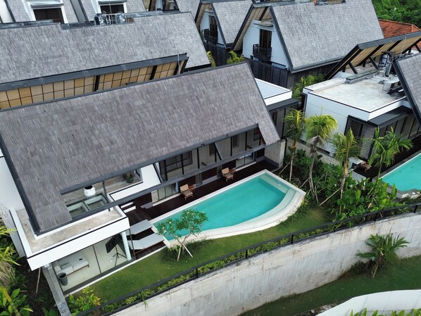 Un bâtiment moderne à plusieurs étages, doté d’une piscine, d’un espace extérieur aménagé et d’une végétation luxuriante.