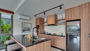 A modern kitchen with wooden cabinets, a stainless steel sink, and a built-in island with bar stools. - Villa Pasisi 11 - Canggu (Canggu)