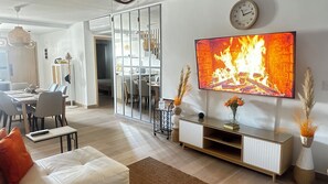 Una sala de estar moderna con un televisor de pantalla plana, un sofá, un comedor y una cocina al fondo.