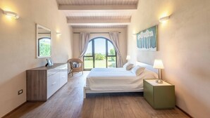 Une chambre à coucher avec un lit, une table de chevet et une commode. Il y a une fenêtre avec des rideaux, une chaise et un tableau au mur.