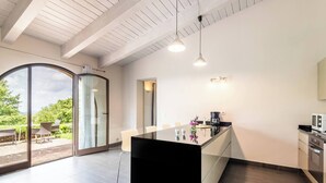 Une cuisine moderne dotée d’un grand îlot central, de portes-fenêtres coulissantes donnant sur un espace extérieur et d’une table à manger avec des chaises.
