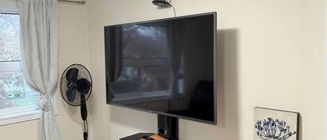 Ein Wohnzimmer mit einem Wand-Fernseher, einem Standventilator, einer schwarzen Unterhaltungseinheit und einem Gemälde an der Wand.