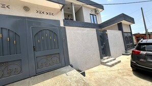 A modern two-story house with a grey facade, a gated entrance, and a visible staircase leading to the upper floor. - Mariagletta Cozy Villa (Abomey Calavi)