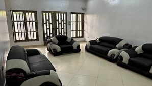 A spacious living room with a large sofa set, a coffee table, and a TV. There are large windows with bars, allowing natural light. - Mariagletta Cozy Villa (Abomey Calavi)