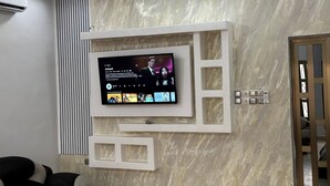 A modern living room with a large flat-screen TV mounted on a marble wall, a built-in fireplace, and a door leading to another room. - Mariagletta Cozy Villa (Abomey Calavi)