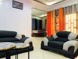 A living room with two sofas, a dining table, and a TV. - Mariagletta Cozy Villa (Abomey Calavi)