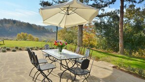 Un patio con una mesa, sillas, un paraguas grande y un jarrón con flores.