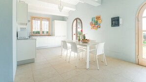 Una cocina luminosa con armarios blancos, una mesa de comedor con sillas y un ventanal con cortinas.