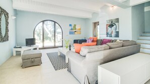 Una sala de estar moderna con un sofá gris, una mesita con un televisor y un ventanal grande.