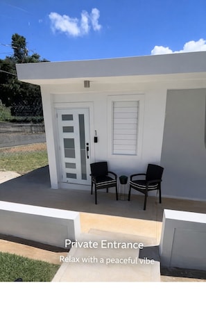 Ein privater Eingang mit weißer Fassade, zwei schwarzen Stühlen und einem kleinen Tisch.