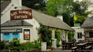 Een wit gebouw met een bord waarop 'Kate Kearney's Cottage' staat, en een bord met 'Restaurant' eronder.