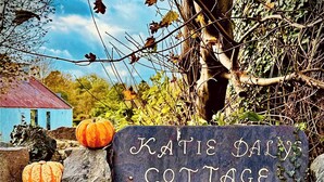Een stenen muur met een bord waarop staat: Katie Daly's Cottage.