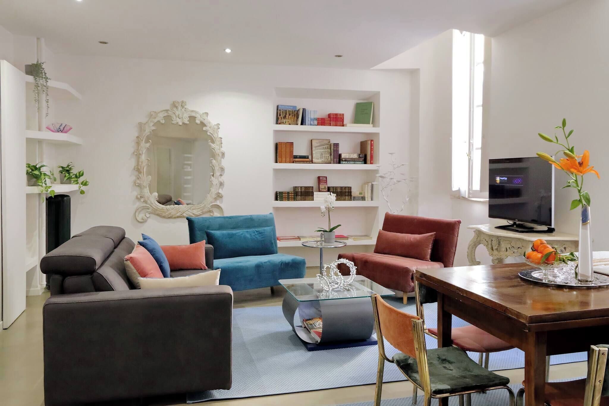A modern living room with a sofa, chairs, a coffee table, and a TV. There are bookshelves with books and decorative items.