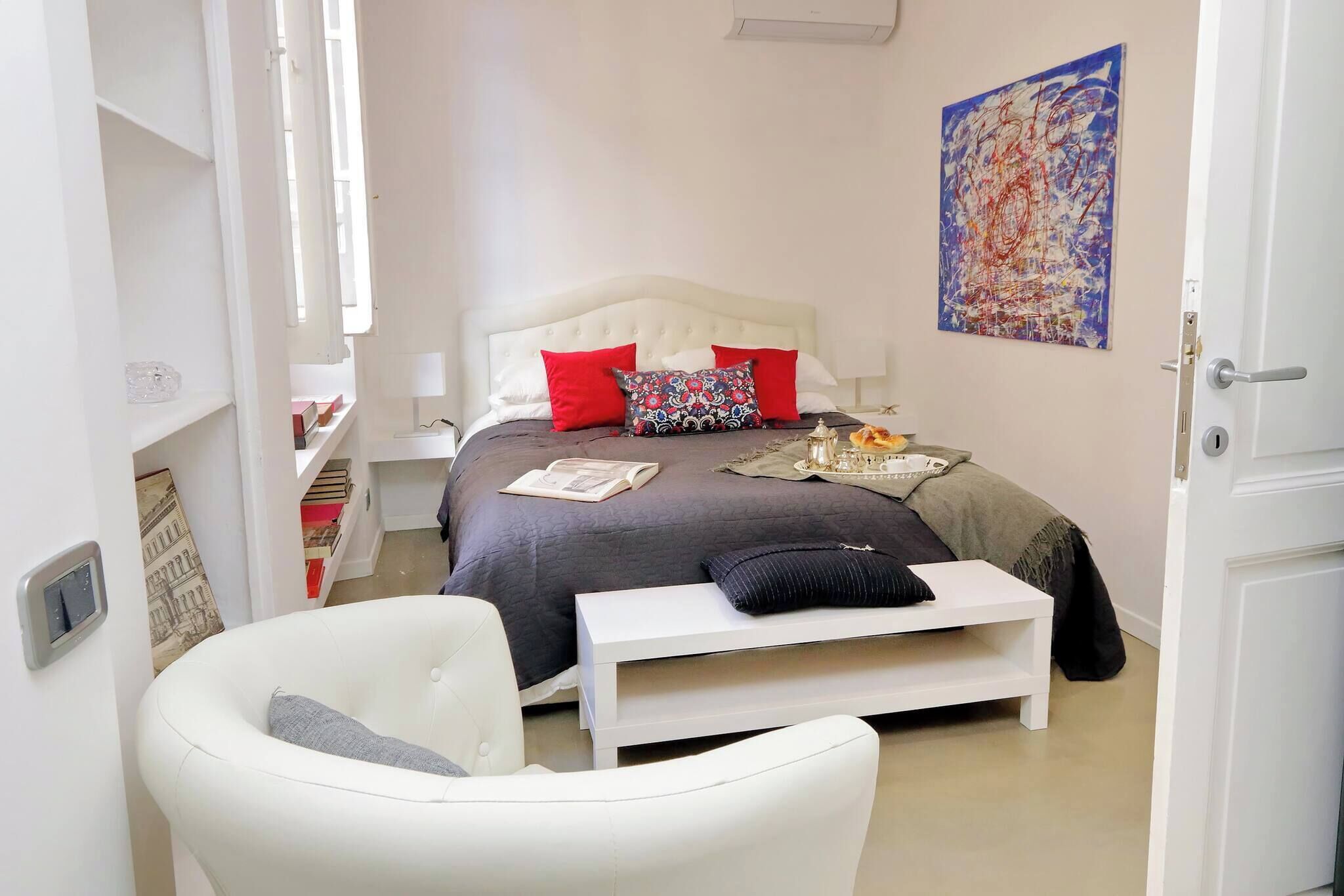 A bedroom with a bed, bedside table, chair, and a painting on the wall.