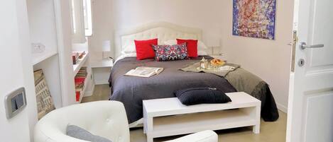A bedroom with a bed, bedside table, chair, and a painting on the wall.